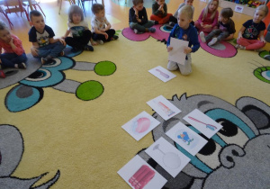 Chłopiec z pośród innych ilustracji wybiera szczotkę do włosów, w tle siedzą na dywanie dzieci.